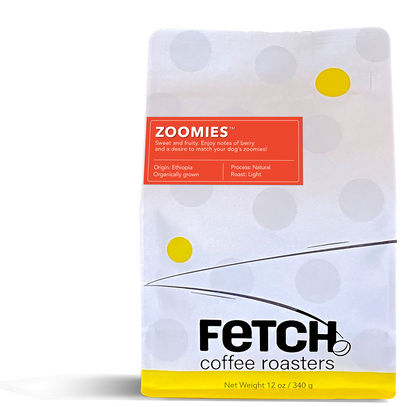 Zoomies has a red-orange label offset to the left and toward the top of the white reclosable coffee bag. The bottom of the bag has a yellow band, and the logo shows a bean sitting at the base of the 'h' of the word Fetch.