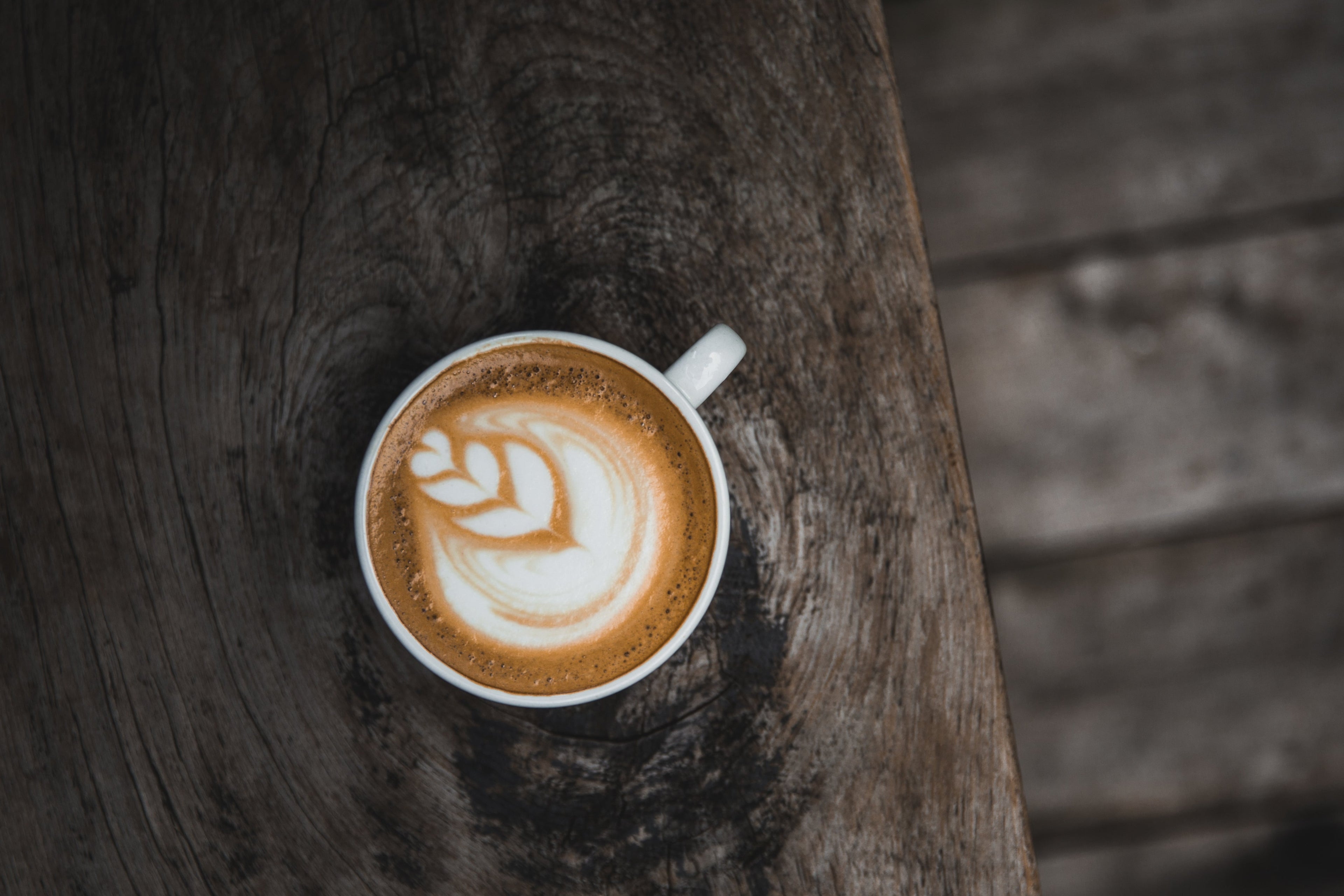 White ceramic cup with tulip latte art  latte sitting on a dark brown wooden table